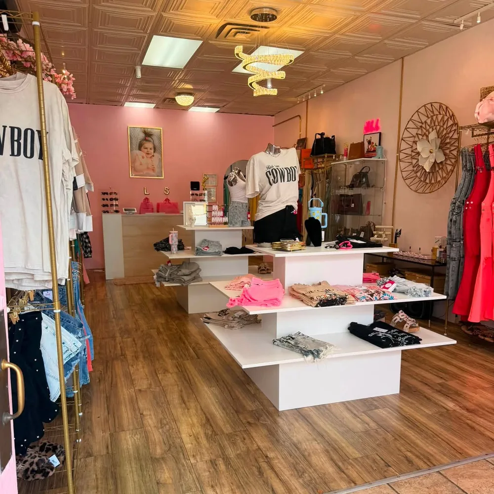 Inside the shop: gold spiral chandeliers, a pressed tin ceiling, brass rails, white display tables and a blush pink back wall.